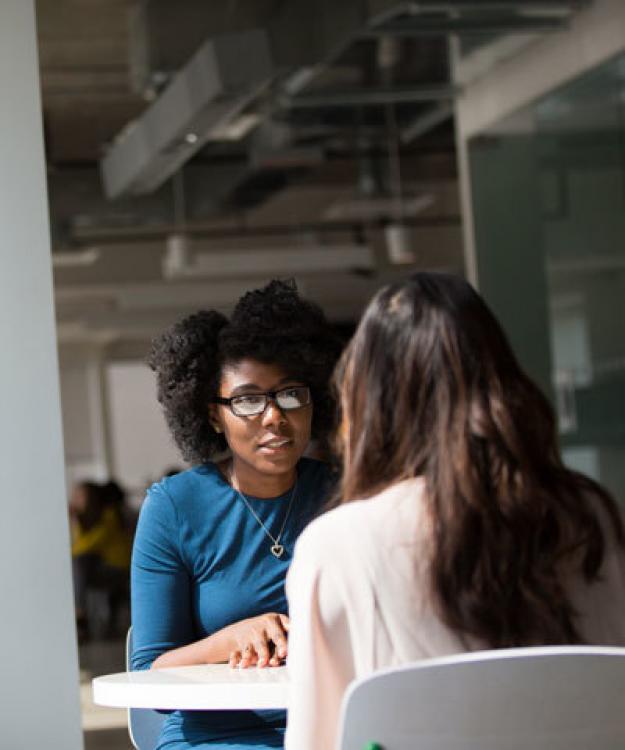 Two young women talking to each other at a table